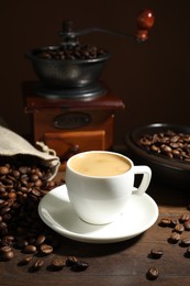 Photo of Aromatic coffee in cup, beans and grinder on wooden table against brown background