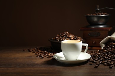 Photo of Aromatic coffee in cup, beans and grinder on wooden table against brown background, space for text
