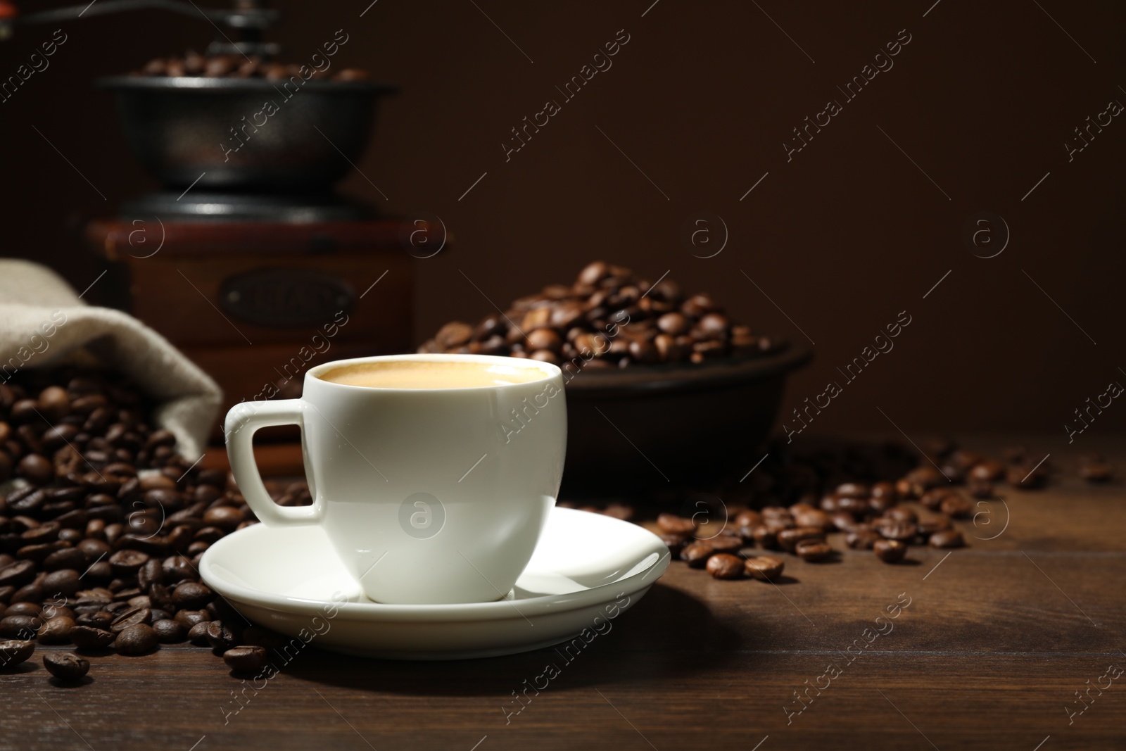 Aromatic coffee in cup, beans and grinder on wooden table against brown background, closeup Photo of Aromatic coffee in cup, beans and grinder on wooden table against brown background, closeup