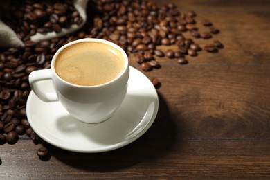 Photo of Aromatic coffee in cup and beans on wooden table, closeup. Space for text