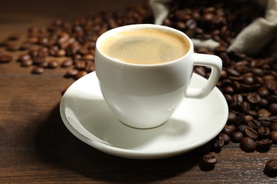Photo of Aromatic coffee in cup and beans on wooden table, closeup