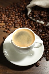 Photo of Aromatic coffee in cup and beans on wooden table, closeup