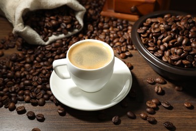Photo of Aromatic coffee in cup and beans on wooden table, closeup