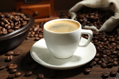 Photo of Aromatic coffee in cup and beans on wooden table, closeup
