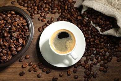 Photo of Aromatic coffee in cup and beans on wooden table, flat lay