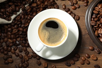 Photo of Aromatic coffee in cup and beans on wooden table, flat lay