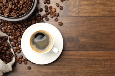 Photo of Aromatic coffee in cup and beans on wooden table, flat lay. Space for text