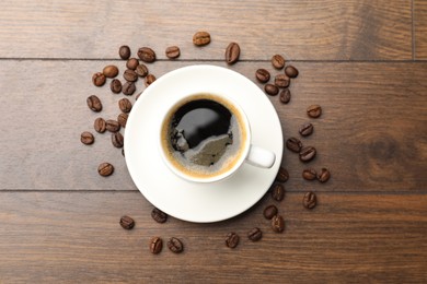 Photo of Aromatic coffee in cup and beans on wooden table, flat lay