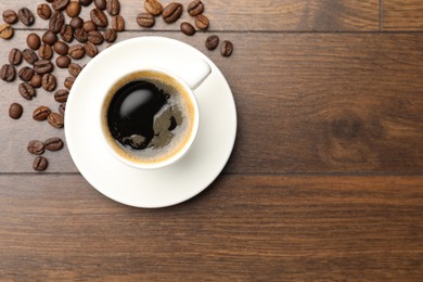 Photo of Aromatic coffee in cup and beans on wooden table, flat lay. Space for text