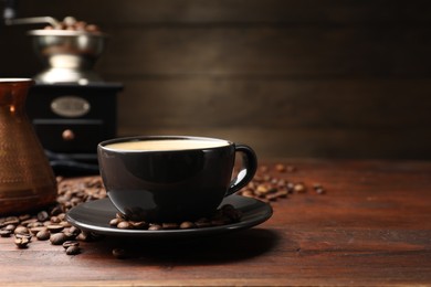 Photo of Aromatic coffee in cup, beans, cezve and grinder on wooden table, closeup. Space for text