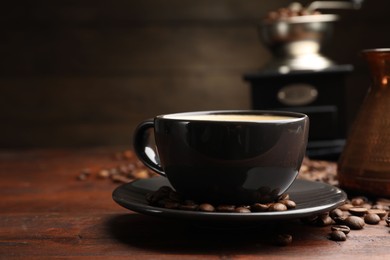 Photo of Aromatic coffee in cup, beans, cezve and grinder on wooden table, closeup
