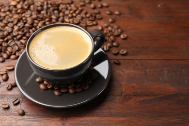 Photo of Aromatic coffee in cup and beans on wooden table, closeup. Space for text
