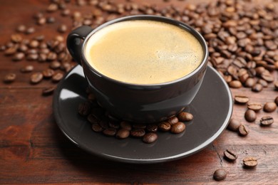 Photo of Aromatic coffee in cup and beans on wooden table, closeup