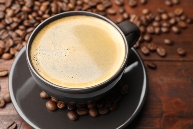 Photo of Aromatic coffee in cup and beans on wooden table, closeup