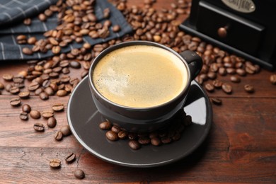 Photo of Aromatic coffee in cup, beans and grinder on wooden table, closeup