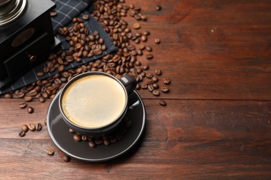 Photo of Aromatic coffee in cup, beans and grinder on wooden table, above view. Space for text