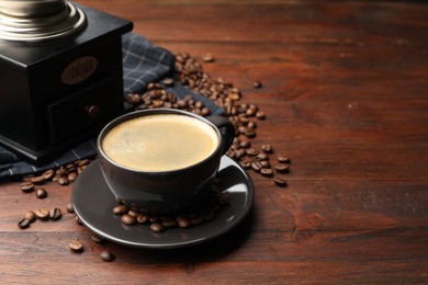Photo of Aromatic coffee in cup, beans and grinder on wooden table, closeup. Space for text