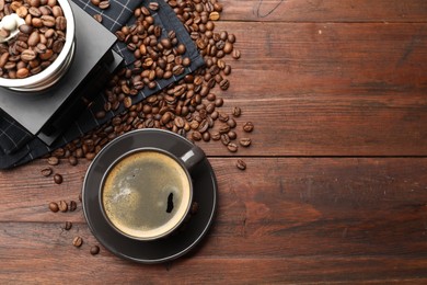 Photo of Aromatic coffee in cup, beans and grinder on wooden table, flat lay. Space for text