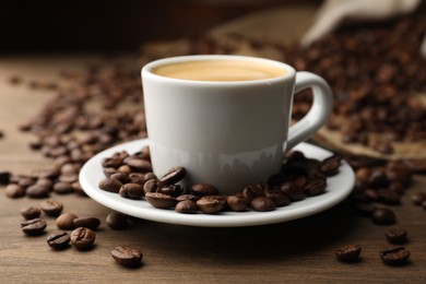 Photo of Aromatic coffee in cup and beans on wooden table, closeup