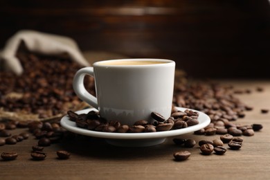 Photo of Aromatic coffee in cup and beans on wooden table, closeup