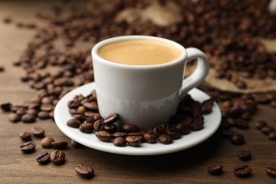 Photo of Aromatic coffee in cup and beans on wooden table, closeup