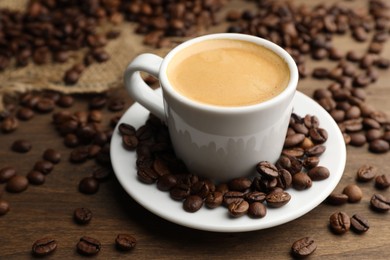 Photo of Aromatic coffee in cup and beans on wooden table, closeup