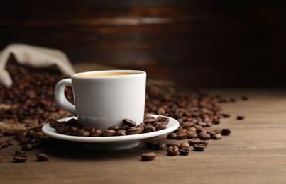 Photo of Aromatic coffee in cup and beans on wooden table, closeup. Space for text