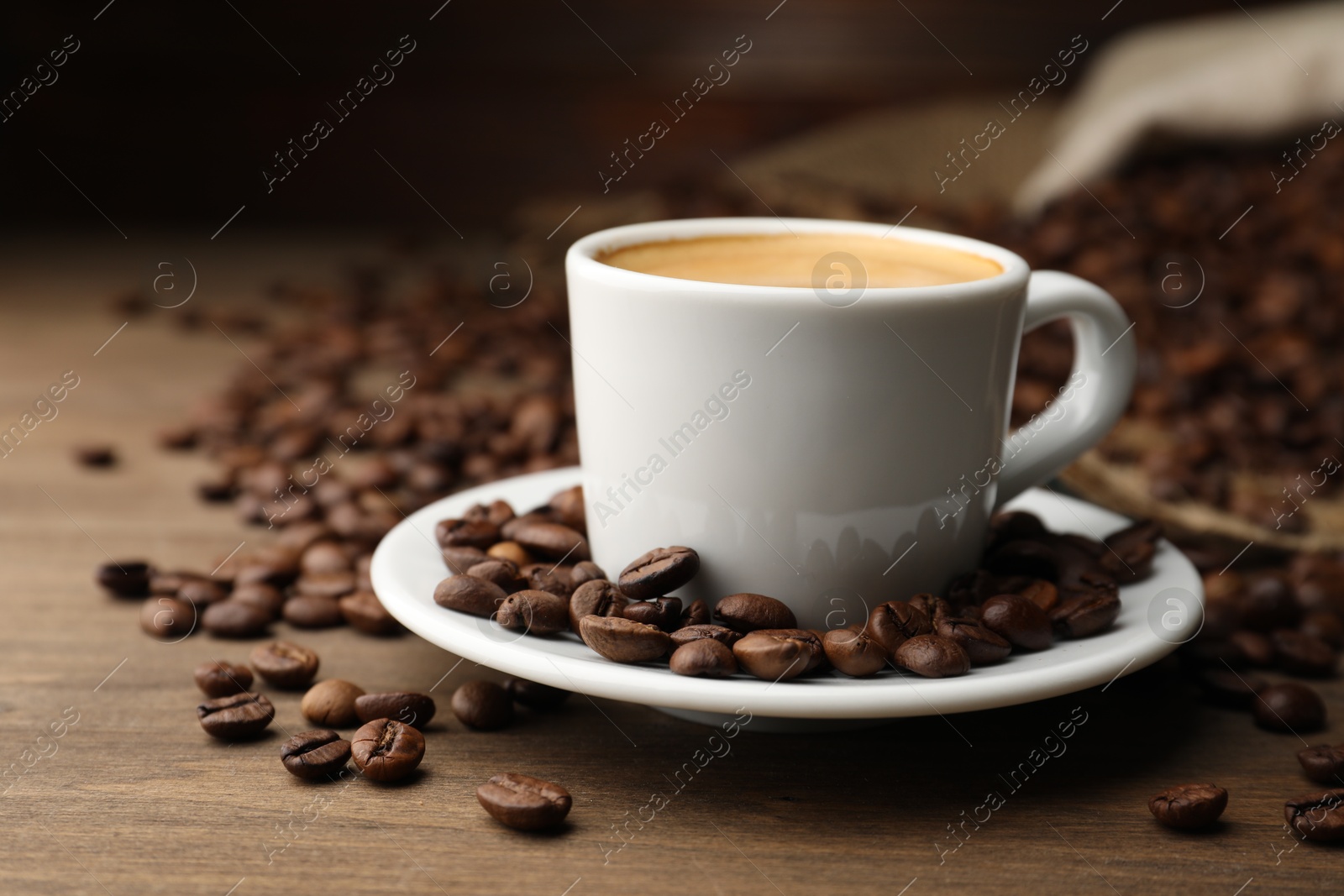 Aromatic coffee in cup and beans on wooden table, closeup Photo of Aromatic coffee in cup and beans on wooden table, closeup