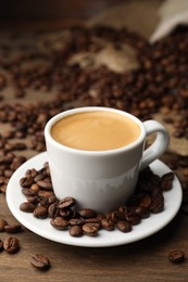 Photo of Aromatic coffee in cup and beans on wooden table, closeup