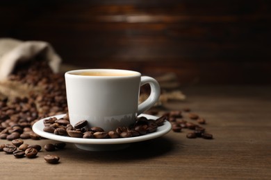 Photo of Aromatic coffee in cup and beans on wooden table, closeup. Space for text