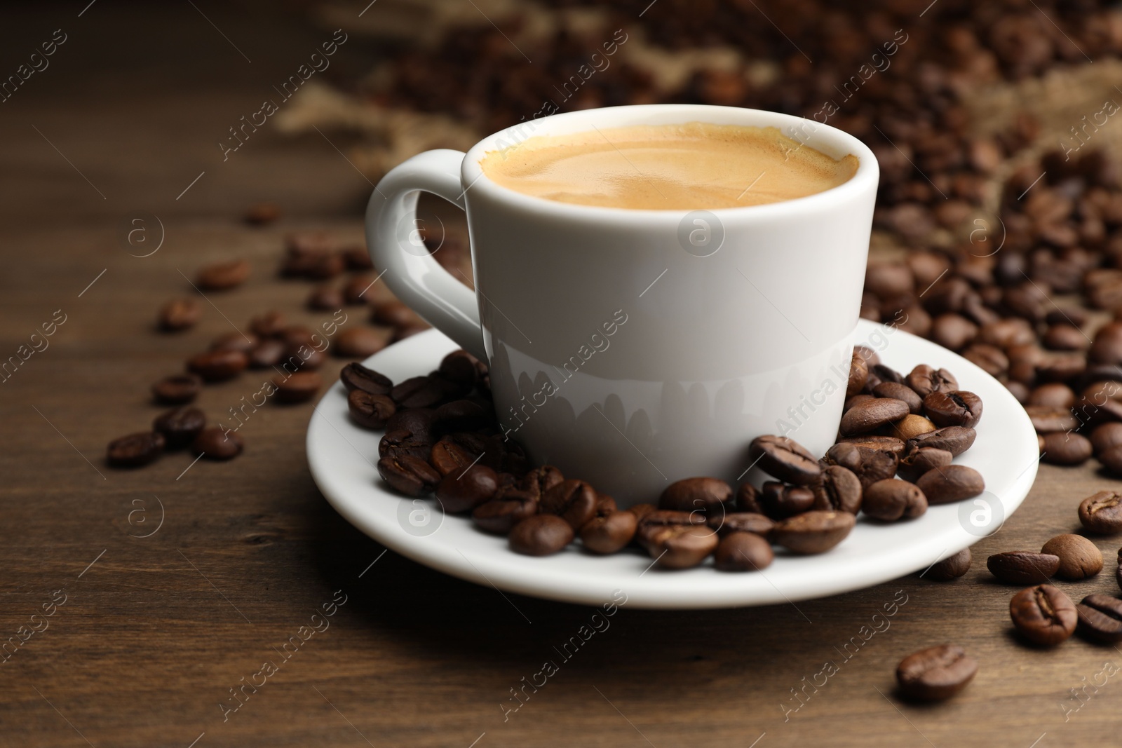 Aromatic coffee in cup and beans on wooden table, closeup Photo of Aromatic coffee in cup and beans on wooden table, closeup