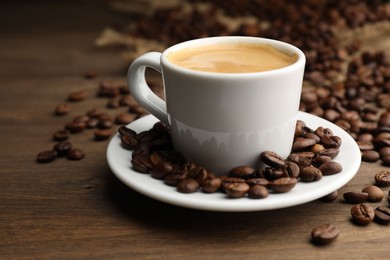 Photo of Aromatic coffee in cup and beans on wooden table, closeup