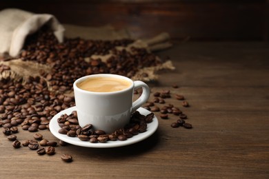 Photo of Aromatic coffee in cup and beans on wooden table, space for text