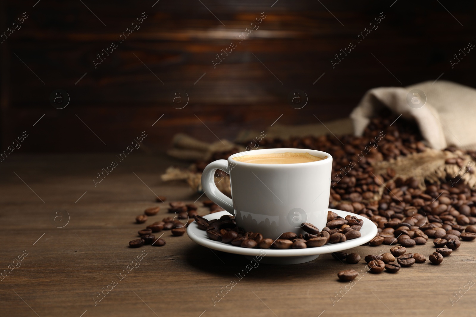 Aromatic coffee in cup and beans on wooden table, space for text Photo of Aromatic coffee in cup and beans on wooden table, space for text