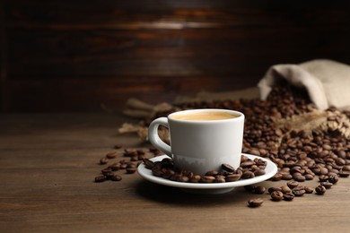 Photo of Aromatic coffee in cup and beans on wooden table, space for text