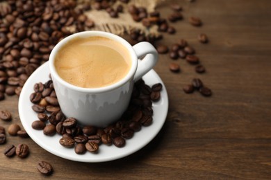 Photo of Aromatic coffee in cup and beans on wooden table, closeup. Space for text
