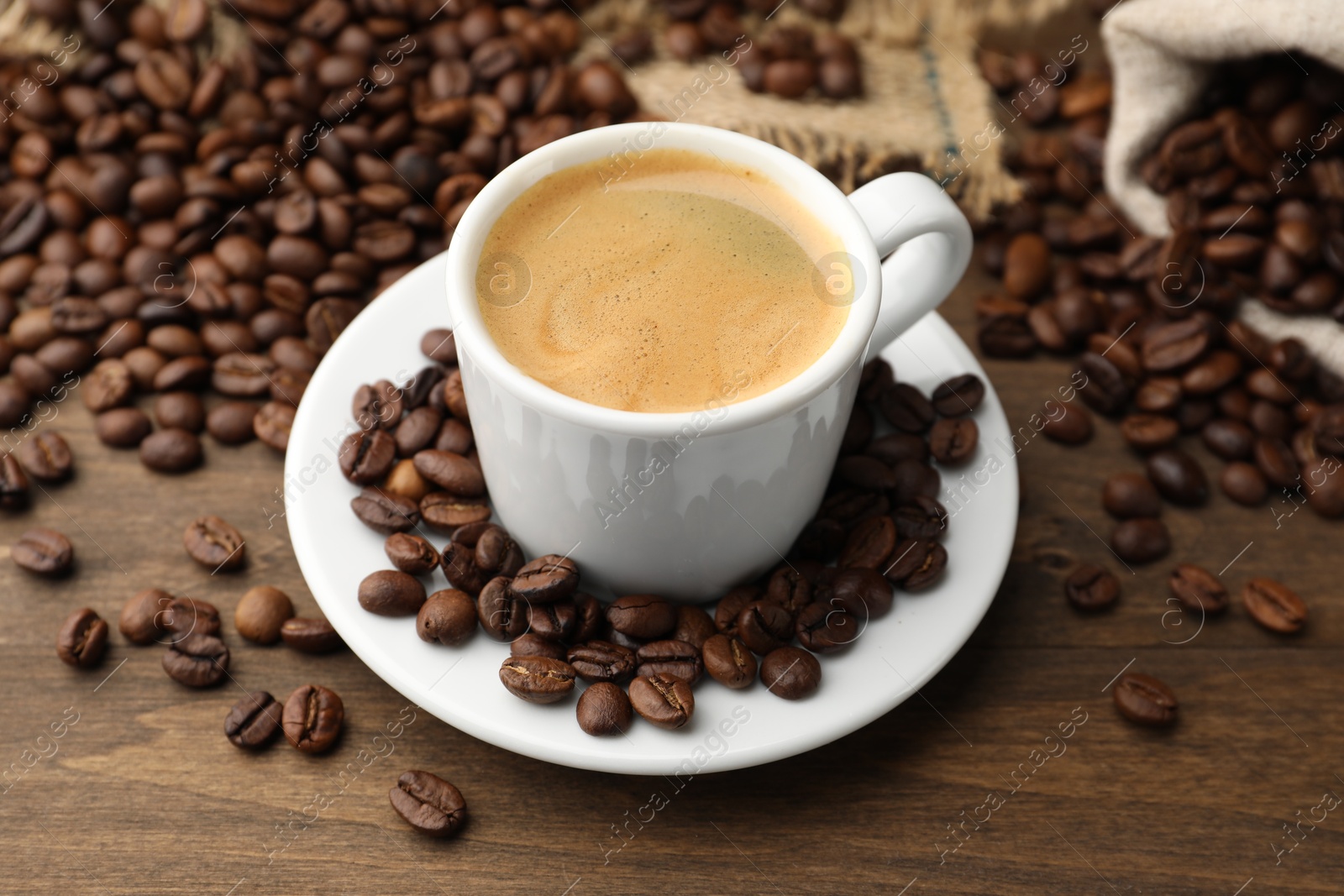 Aromatic coffee in cup and beans on wooden table, closeup Photo of Aromatic coffee in cup and beans on wooden table, closeup