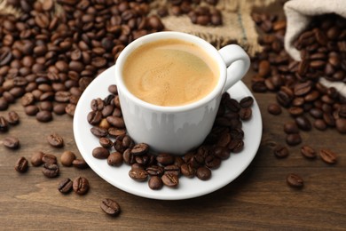 Photo of Aromatic coffee in cup and beans on wooden table, closeup