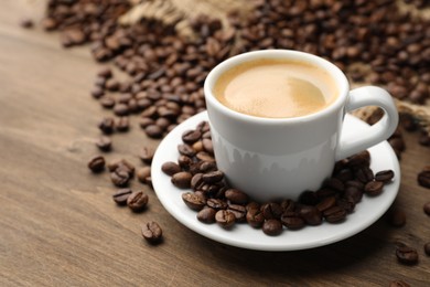 Photo of Aromatic coffee in cup and beans on wooden table, closeup. Space for text