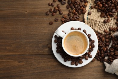 Photo of Aromatic coffee in cup and beans on wooden table, flat lay. Space for text