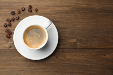 Photo of Aromatic coffee in cup and beans on wooden table, flat lay. Space for text