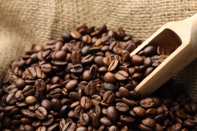 Photo of Aromatic coffee beans and scoop in burlap bag, closeup
