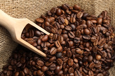 Photo of Aromatic coffee beans and scoop in burlap bag, above view