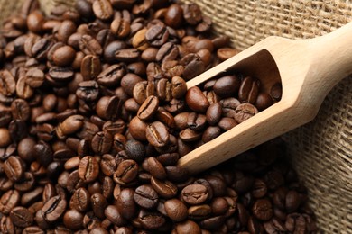 Photo of Aromatic coffee beans and scoop in burlap bag, closeup