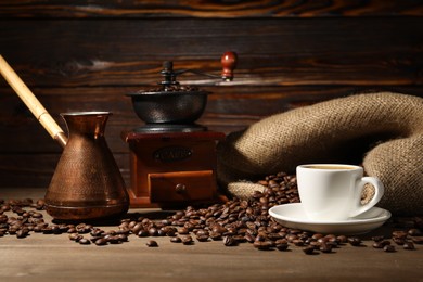 Photo of Aromatic coffee in cup, beans, cezve and grinder on wooden table