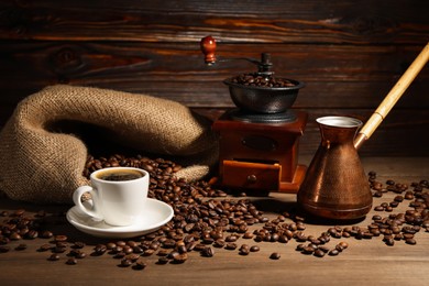 Photo of Aromatic coffee in cup, beans, cezve and grinder on wooden table