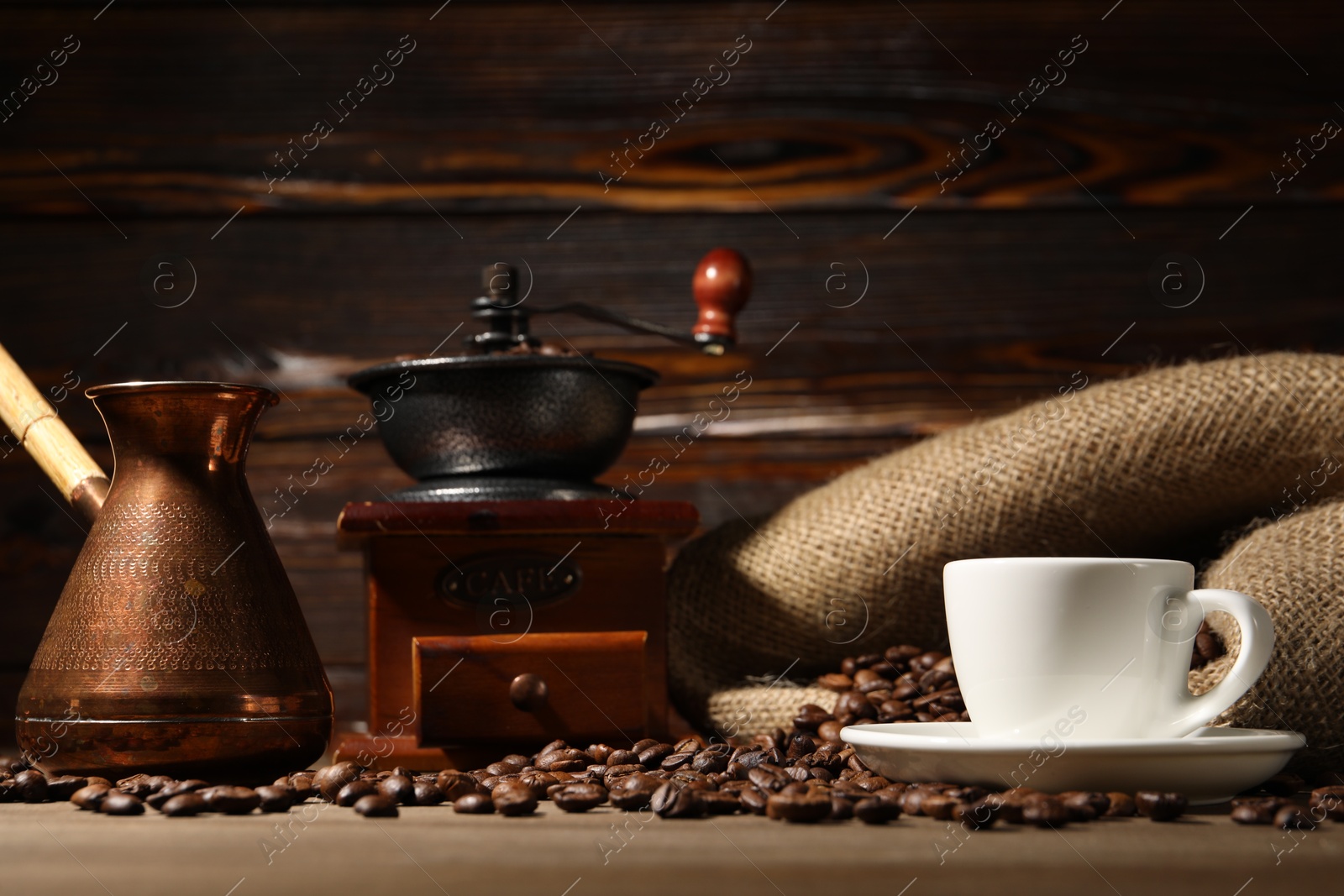 Photo of Cup of drink, coffee beans, cezve and grinder on wooden table