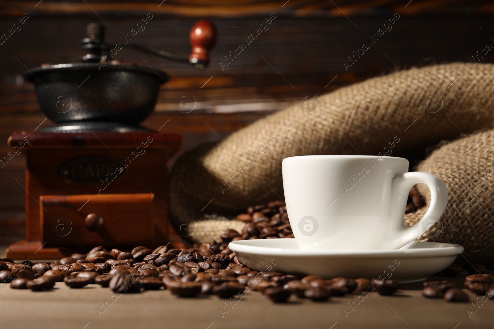 Photo of Cup of drink, coffee beans and grinder on wooden table, closeup
