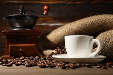Photo of Cup of drink, coffee beans and grinder on wooden table, closeup