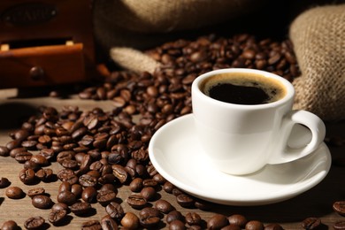 Photo of Aromatic coffee in cup and beans on wooden table, closeup